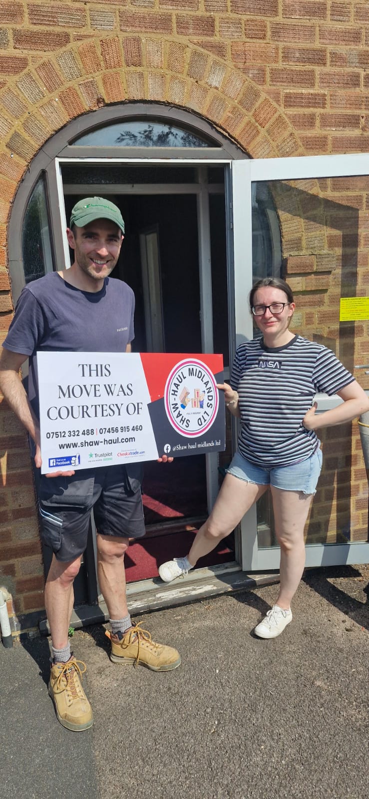 Couple holding the Shaw Haul move sign at their arched front door