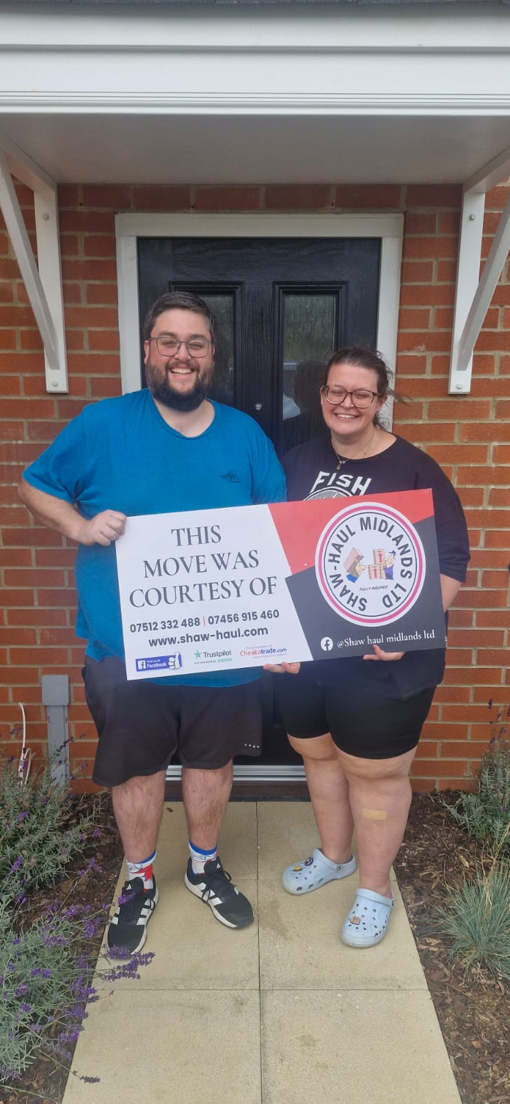 Smiling couple holding the Shaw Haul move sign at their front door