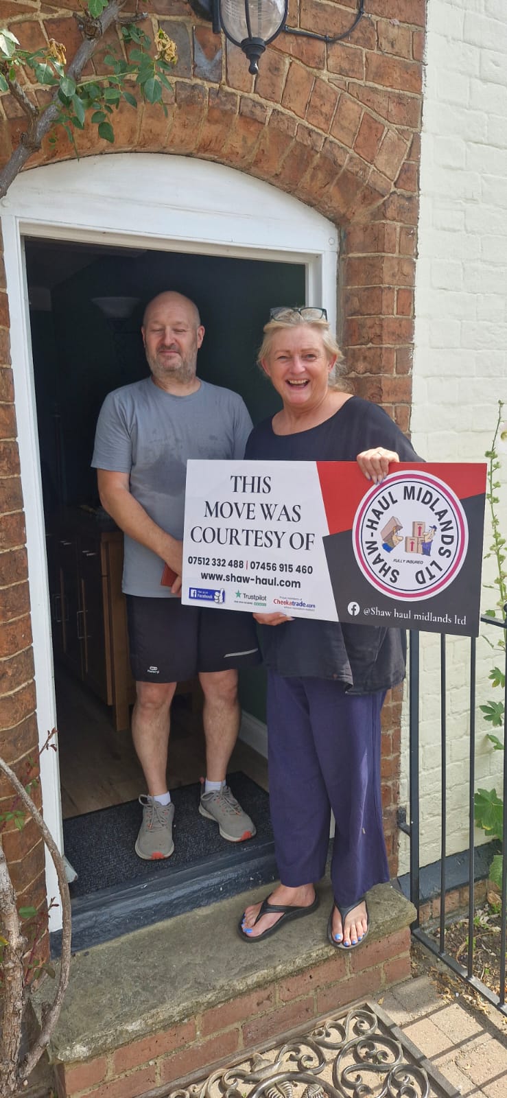 Couple at an arched brick doorway holding the Shaw Haul move sign