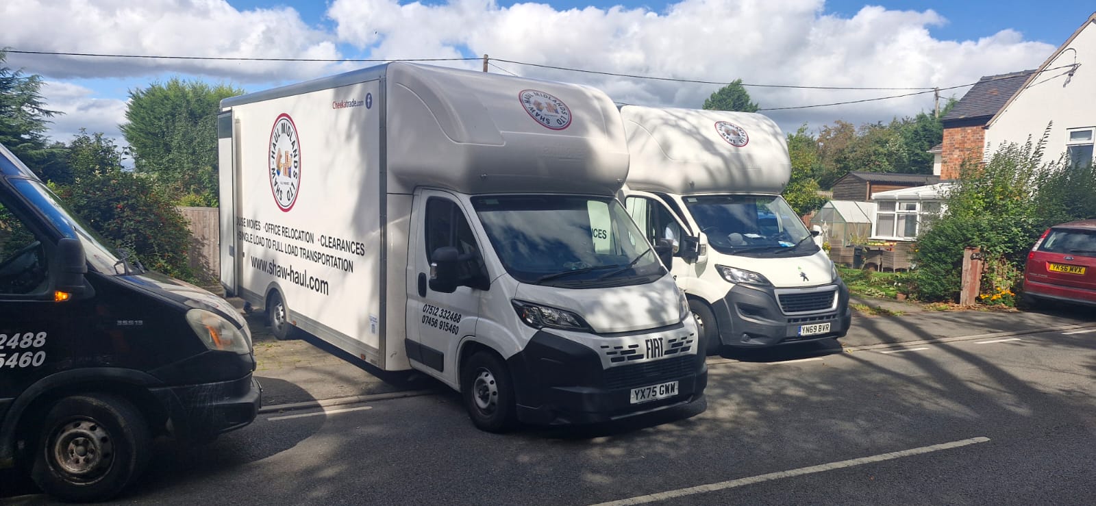 Two Shaw Haul Luton vans and a black van lined up on a village street